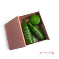 Coffret beauté cheveux Ziaja à l’huile d’olive dans une boîte rose ouverte, contenant un shampoing, un après-shampoing et un masque capillaire verts. Logo Ply’Beauty en bas de l’image.